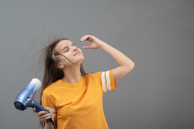 Mädchen trocknet Haare mit einem Haartrockner auf einem grauen Hintergrund lächelnd