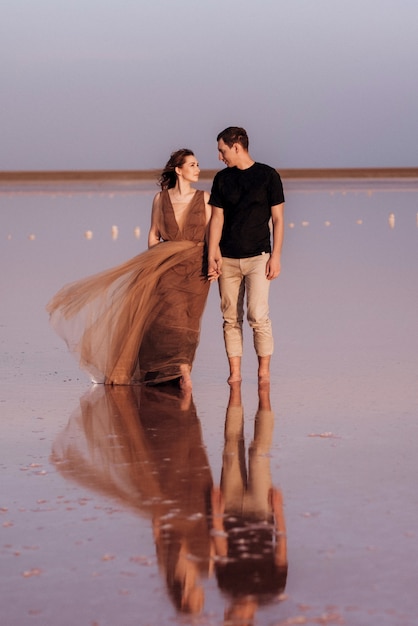 Mädchen und ein Mann am Ufer eines rosa Salzsees bei Sonnenuntergang