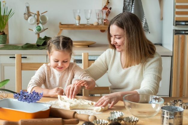 Mädchen und Frau kochen zu Hause in einer Küche ein Kind rührt Mehl und knetet den Teig auf dem Tisch von Hand