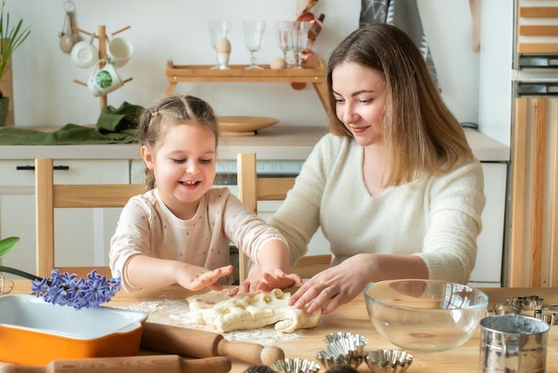 Mädchen und Frau kochen zu Hause in einer Küche ein Kind rührt Mehl und knetet den Teig auf dem Tisch von Hand