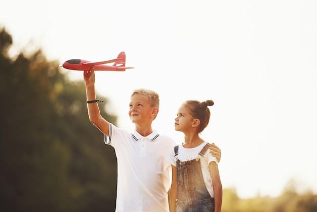Foto mädchen und junge, die sich im freien mit rotem spielzeugflugzeug in den händen amüsieren.