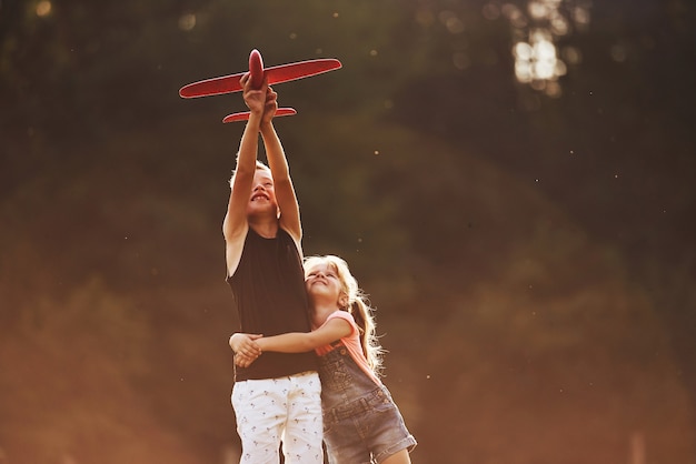 Mädchen und Junge, die sich im Freien mit rotem Spielzeugflugzeug in den Händen amüsieren.