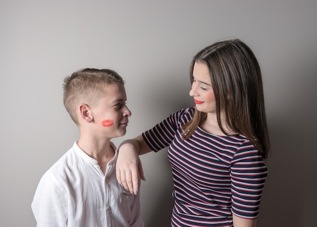 Mädchen und Junge mit Lippenstift küssen sich auf seinem Gesicht auf hellem Hintergrund