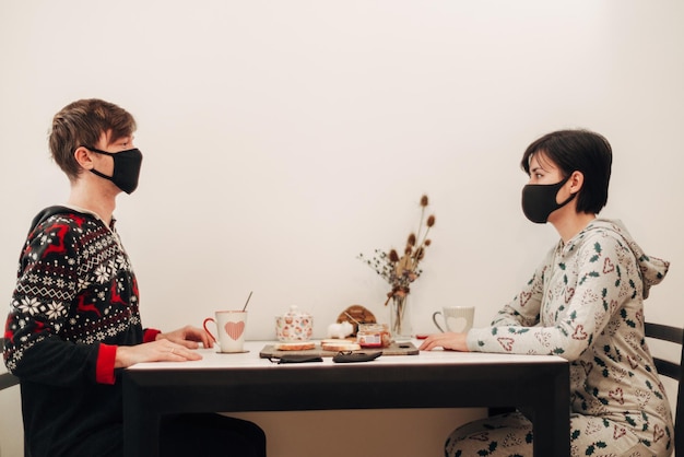 Mädchen und Kerl, die zu Hause Tee in Masken trinken