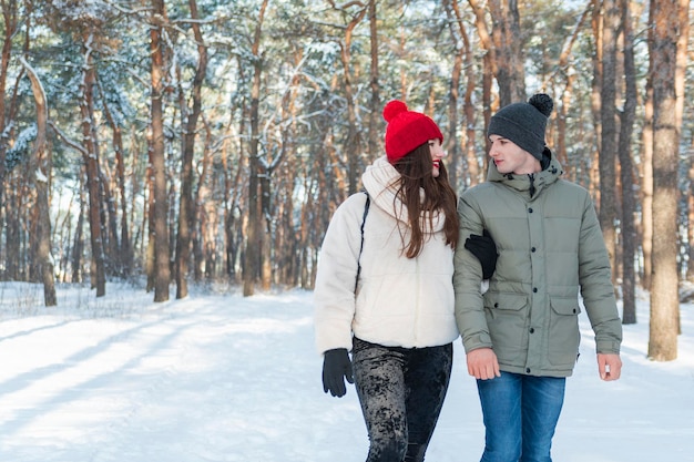 Mädchen und Kerl gehen in den Winterpark Junges Paar im verschneiten Wald