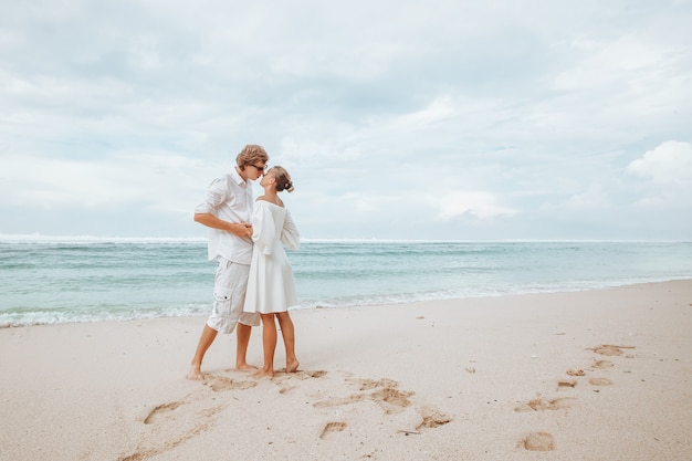 Mädchen und Kerl in weißen Kleidern, weißer Strand und Umarmung