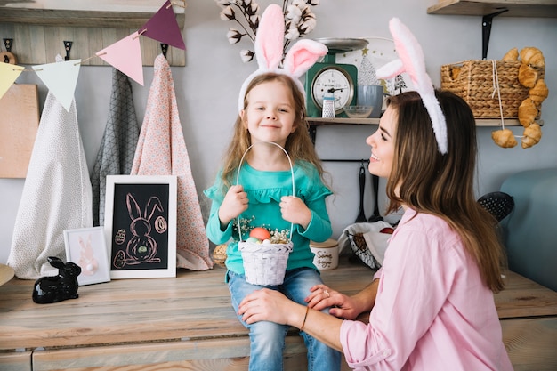 Foto mädchen und mutter in den häschenohren, die mit korb von ostereiern sitzen