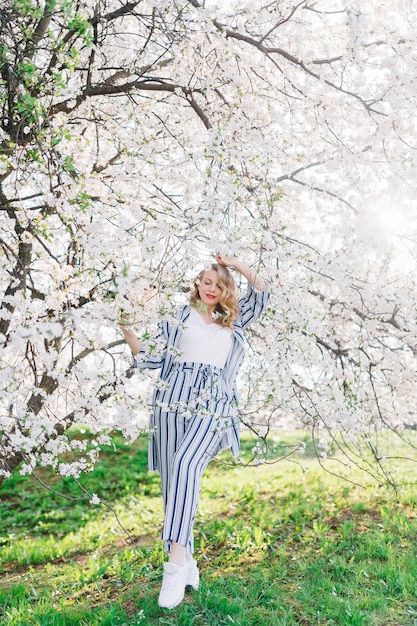 Mädchen unter Blütenbaum. Junge Frau, die im Blumengarten im Frühling lächelt. Sommermode-Konzept