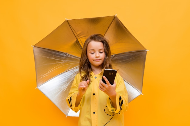 Mädchen unter einem offenen Regenschirm sitzt am Telefon auf einem gelben Hintergrund