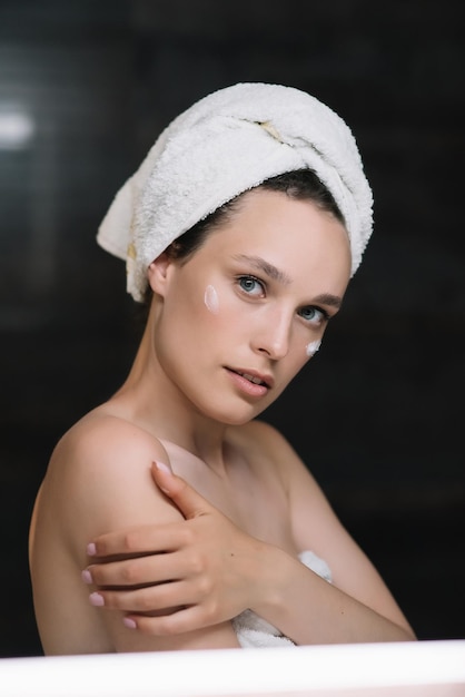 Mädchen wenden revitalisierende Gesichtscreme oder Maske im Badezimmer an, schauen in die Kamera und berühren ihre Haut
