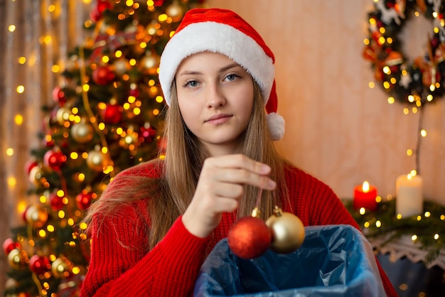 Mädchen wirft Christbaumkugeln in den Papierkorb weg Verwenden Sie Weihnachtsschmuck nur einmal und kaufen Sie dann neu