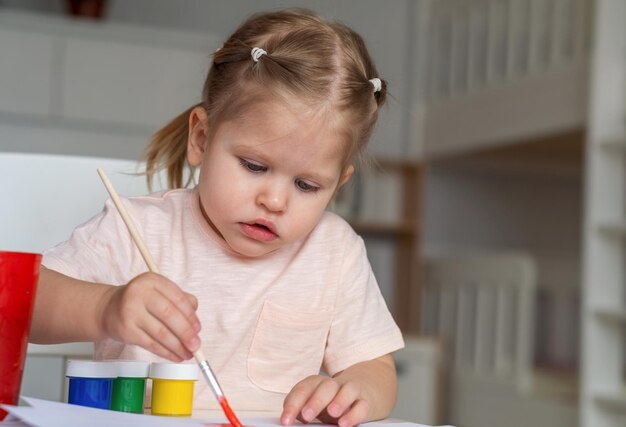 Mädchen zeichnet eine Kinderzeichnung mit Farben und Pinsel