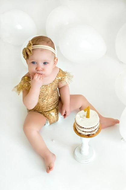 Mädchen zerquetscht den ersten Kuchen am Geburtstag auf weißem Hintergrund mit Luftballons