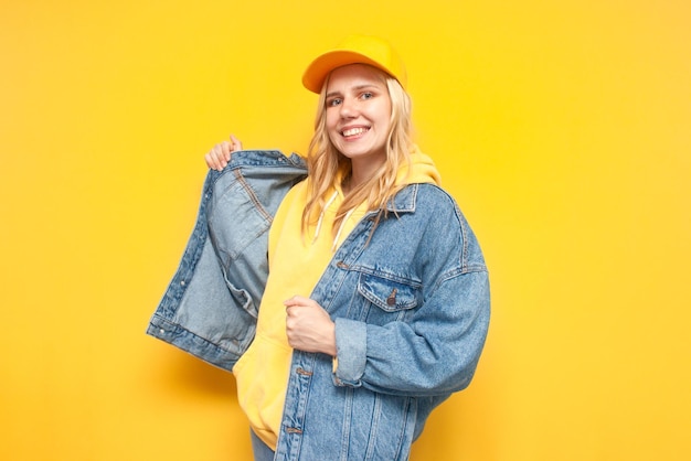 Mädchen zieht eine Jeansjacke auf gelbem Hintergrund an und lächelt