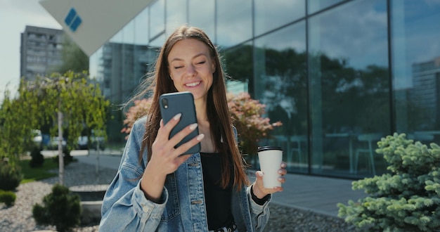 Mädchen zu Fuß mit Smartphone und Kaffeetasse Schöne Frau mit Telefon mit Kaffee zum Mitnehmen auf der Straße