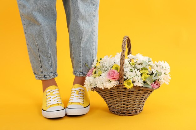 Mädchenbeine und Blumenkorb auf gelbem Hintergrund