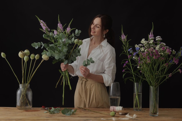 Mädchenflorist sammelt einen Blumenstrauß in einer Blumenwerkstatt auf einem dunklen Hintergrundlayout für Floristik