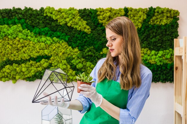 Mädchenfloristengartenpflanzen in der Glasform, Sand, Succulents, Handschuhe, Moos, Innenraum