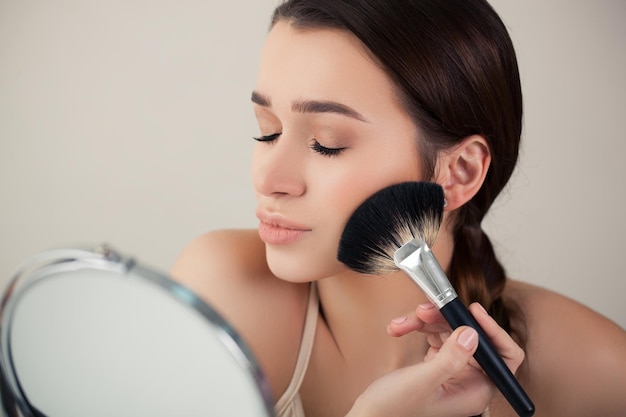 Mädchenfrau im Spiegel macht Make-upbürste