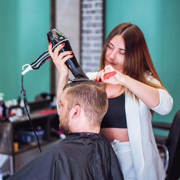 Mädchenfriseur trocknet einem Mann in einem Salon Haar