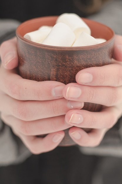 Mädchenhände mit dünnen Fingern halten eine braune Tasse Kaffee mit Marshmallows, getönt und verblasst