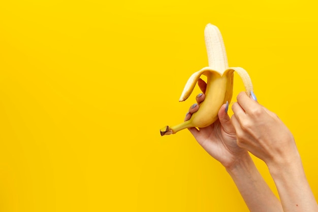 Mädchenhände schälen und öffnen Banane auf gelbem, isoliertem Hintergrund, Nahaufnahme der Frucht