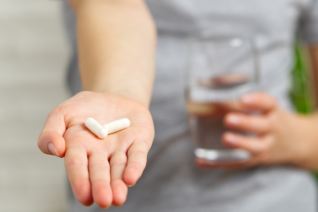 Mädchenhand mit weißen tabletten medizin tabletten und glas wasser