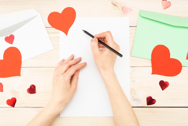 Mädchenhand schreibt einen liebesbrief. valentinstag. handgemachte grußkarte mit einem roten herzen in der form einer figur. der 14. februar ist ein fest der feier. sicht von oben