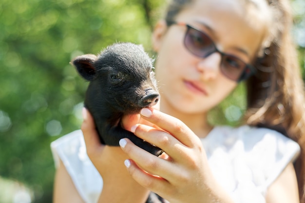 Mädchenkind, das in den Händen des schwarzen neugeborenen Babyferkels hält Bauernhof, Landwirtschaft, Land, Haustiere, Kinderkonzept