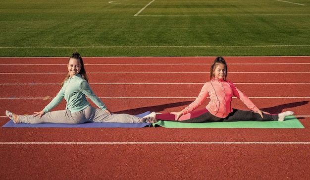 Mädchenkinder, die draußen auf der Stadionarena Sport trainieren, sitzen in Split-Stretching