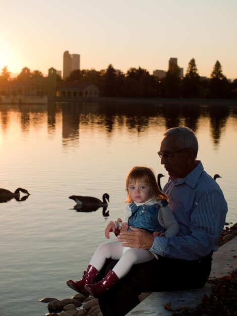 Mädchenkleinkind mit Großvater am See bei Sonnenuntergang.