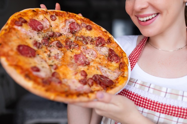 Mädchenkoch lächelt, hält Pizza auf Restauranthintergrund