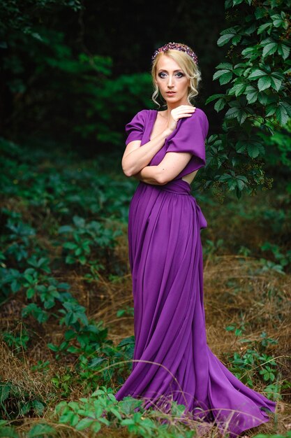 Foto mädchenmodellblondine in einem lila kleid mit einem blumenstrauß mit einem grünen wald