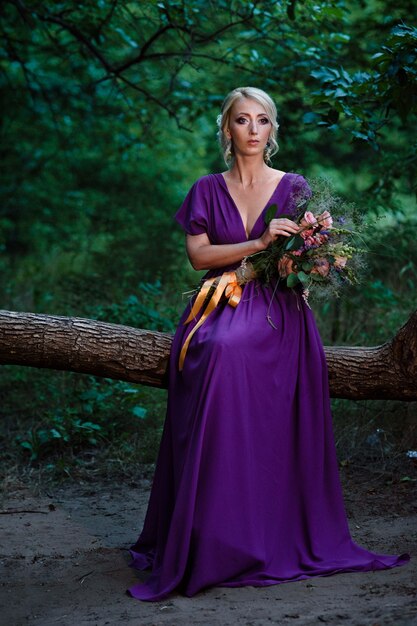 Mädchenmodellblondine in einem lila Kleid mit einem Blumenstrauß mit einem grünen Wald