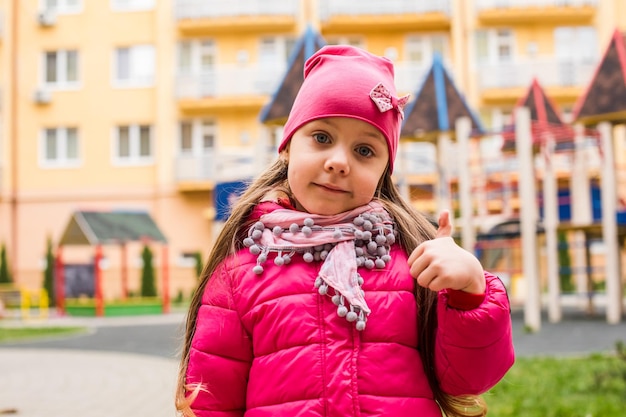 Mädchenporträt mit Daumen nach oben auf dem Spielplatz im Freien Aktives Mädchen liebt es, zu jeder Jahreszeit Zeit im Freien zu verbringen