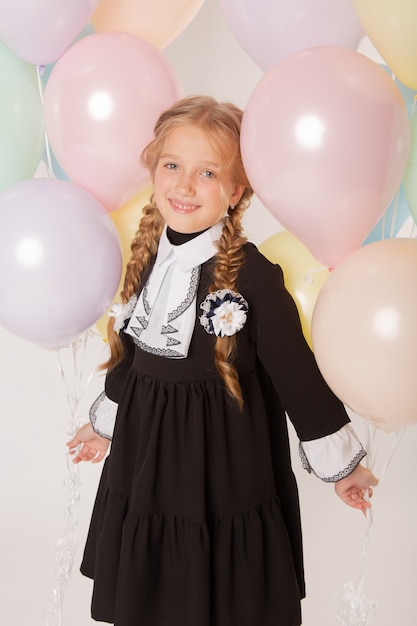 Mädchenschulmädchen, Schülerin der ersten Klasse in Schuluniform auf weißem Hintergrund mit Bällen und Blumen