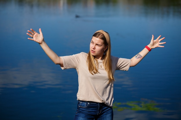 Mädchentanzen in der Nähe des Sees, sonniges Wetter. Eine junge Frau freut sich am Leben, tanzt und singt. Sie hat gute Laune und ein Lächeln im Gesicht.