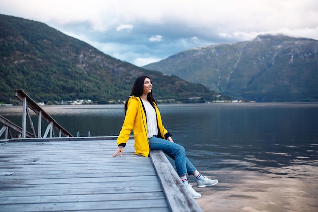 Mädchentourist in der gelben Jacke, die auf dem See in Norwegen aufwirft Aktive Frau, die in Norwegen sich entspannt