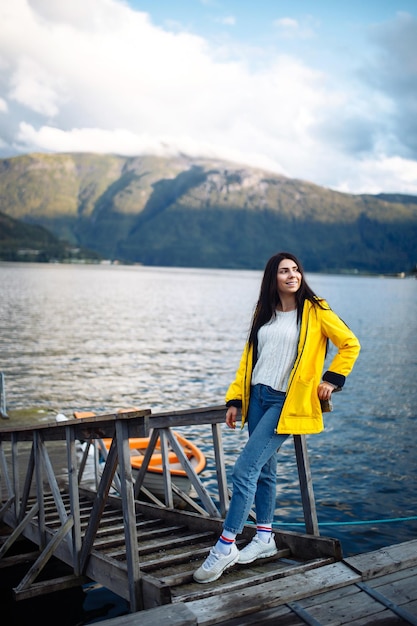 Mädchentourist in einer gelben Jacke, die auf dem See in Norwegen posiert Reisendes Lifestyle-Abenteuer