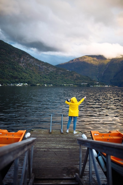 Mädchentourist in einer gelben Jacke, die auf dem See in Norwegen posiert Reisendes Lifestyle-Abenteuer