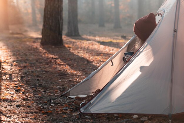 Mädchenwanderer in einem Zelt mit einer Tasse und Wald im Hintergrund