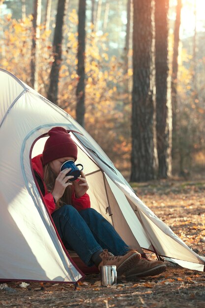 Mädchenwanderer in einem Zelt mit einer Tasse und Wald im Hintergrund