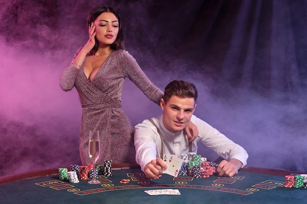 Männchen, das zwei Karten hält, die Poker im Casino spielen, das am Tisch mit Stapeln von Chips darauf sitzt. Er feiert den Sieg mit jungen Mädchen