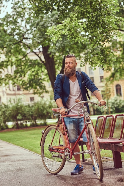 Männchen in lässiger Kleidung, zu Fuß mit einem Retro-Fahrrad in einem Stadtpark.