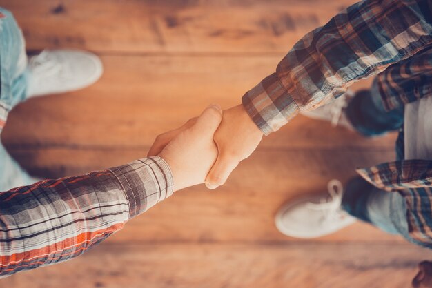 Foto männer beim händeschütteln. draufsicht auf zwei männer, die sich die hände schütteln, während sie auf dem holzboden stehen