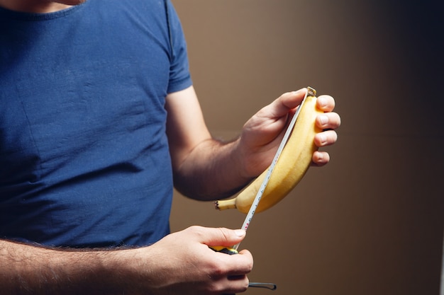 Männer, die Banane auf braunem Hintergrund messen