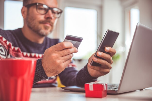 Männer, die Kreditkarte halten und zu Hause Büro des intelligenten Telefons verwenden