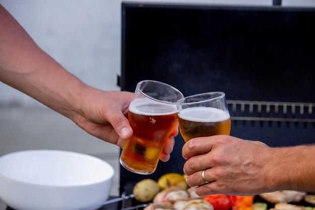 Männer halten Bier in ihren Händen auf dem Hintergrund des Grillgemüses und des Fleisches. Selektiver Fokus auf die Natur