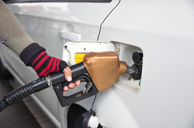 Männer halten Kraftstoffdüse, um Kraftstoff im Auto an der Tankstelle hinzuzufügen