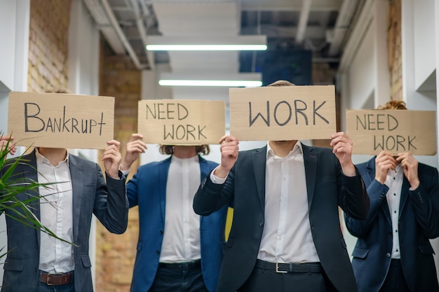 Männer mit hochgezogenen Plakaten, die Arbeit fordern, stehen im Büro, Gesichter sind nicht sichtbar